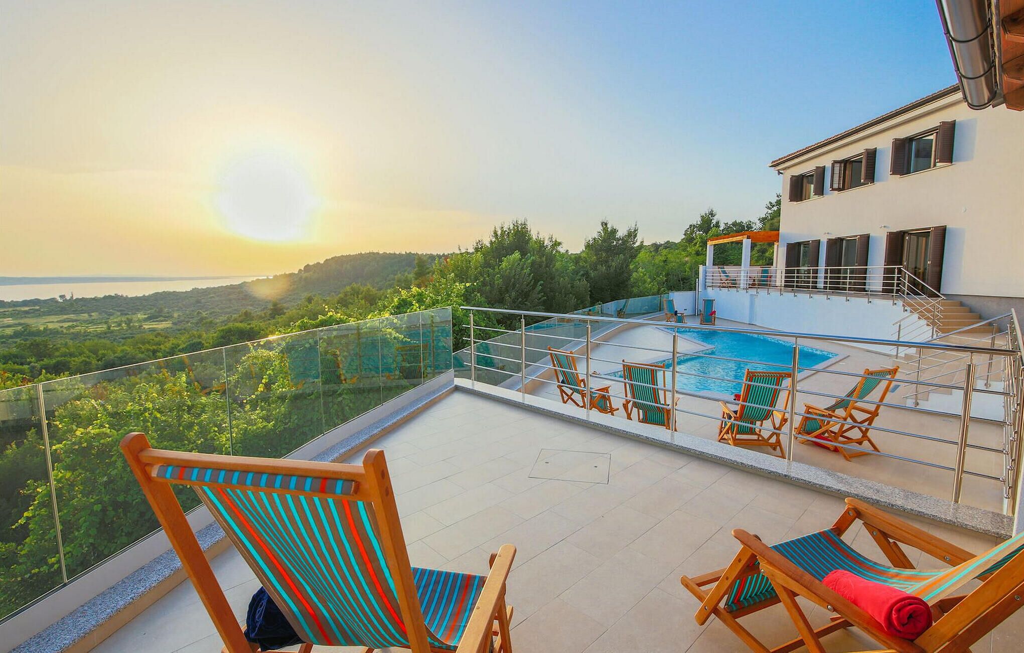 A rooftop terrace with a swimming pool, sun loungers, and a scenic view of the landscape.