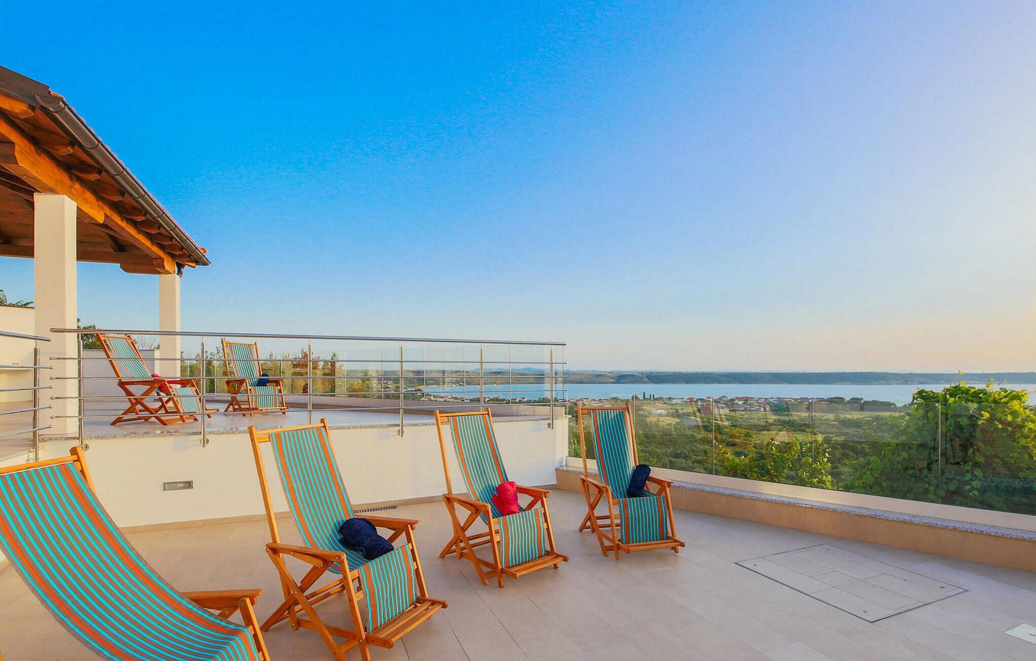 A terrace with wooden chairs and a view of the sea.