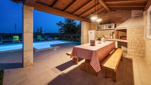 An outdoor patio with a pool, a dining table with a checkered tablecloth, and a stone wall.