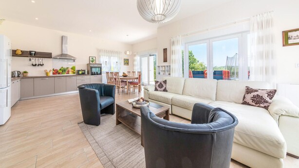 A modern living room with a sofa, two armchairs, a dining area, and a kitchen.