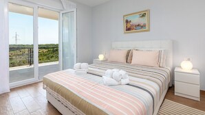 A bedroom with a bed, a nightstand, a painting, and a view of greenery and a power line.