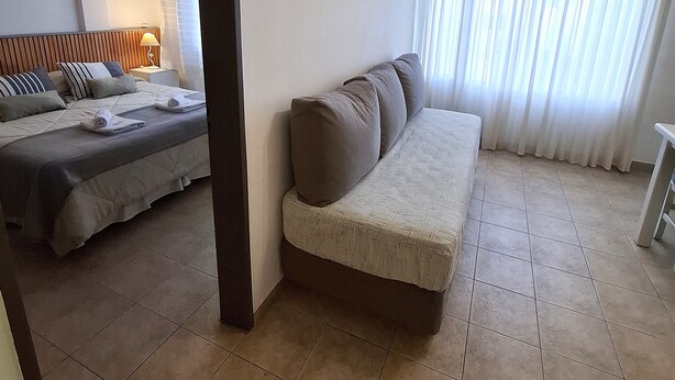 Une pièce avec un lit, un canapé et une grande fenêtre avec des rideaux.