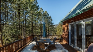 A wooden deck with a table and chairs, surrounded by a forest.