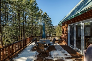 A wooden deck with a table and chairs, surrounded by a forest.