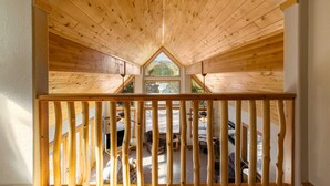 A wooden attic bedroom with a sloped ceiling, a view of the outdoors, and a wooden railing. - Getaway ll by Velo (Angel Fire)