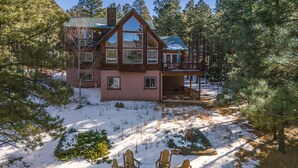 A two-story log cabin with a balcony, surrounded by snow and pine trees. - Getaway ll by Velo (Angel Fire)