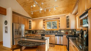 A spacious kitchen with wooden cabinets, granite countertops, stainless steel appliances, and a large island with bar stools. - Getaway ll by Velo (Angel Fire)