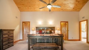 A bedroom with a wooden ceiling fan, a large bed with a wooden headboard, two bedside lamps, and a wooden bench.
