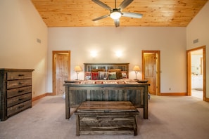 A bedroom with a wooden ceiling fan, a large bed with a wooden headboard, two bedside lamps, and a wooden bench.