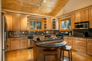 A kitchen with wooden cabinets, granite countertops, a stainless steel refrigerator, a microwave, and a large island with stools.