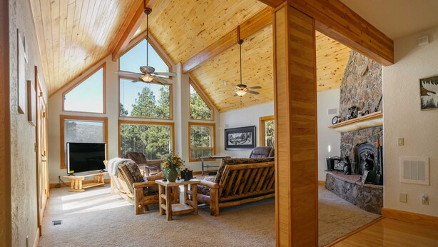 A spacious living room with a high ceiling, large windows, a fireplace, and a television. - Getaway ll by Velo (Angel Fire)
