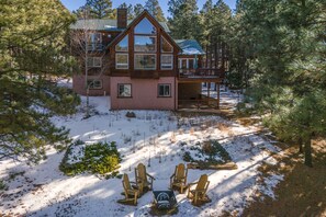Una cabaña de troncos de dos pisos con un porche y un patio cubierto de nieve.
