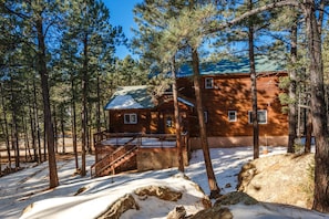 A cabin with a deck and stairs, surrounded by trees and snow.