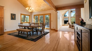 A spacious kitchen with wooden flooring, a dining area with a wooden table and chairs, and large windows allowing natural light.