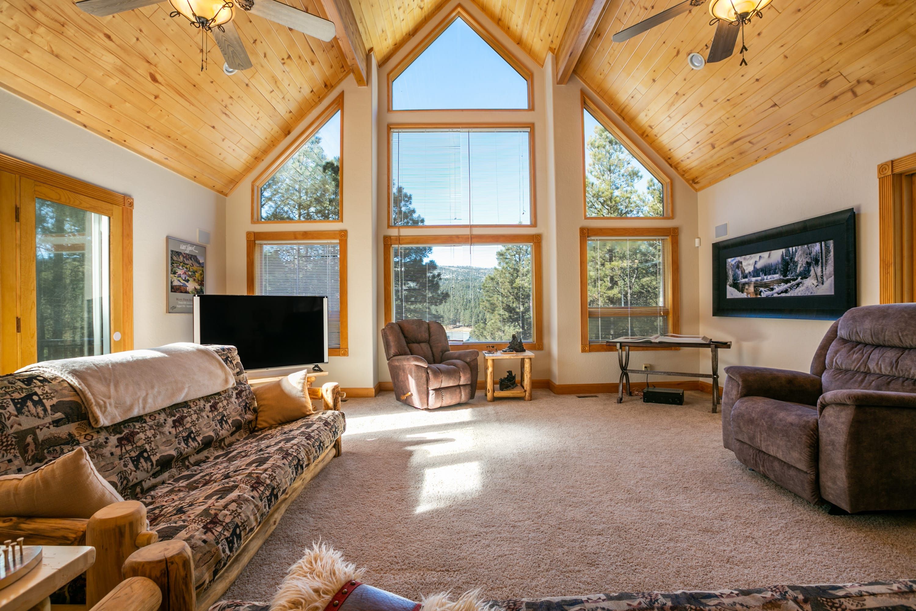 A spacious living room with high ceilings, large windows, a flat-screen TV, and comfortable seating.