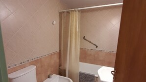Een badkamer met toilet, bidet, bad en douchegordijn.