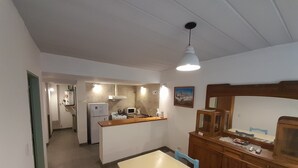Een kleine keuken met een eethoek, voorzien van een koelkast, magnetron, fornuis en houten kastjes.