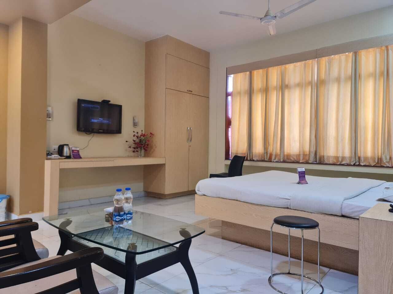 A hotel room with a bed, a glass table, a TV, and a window with curtains.