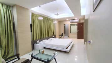 A hotel room with a bed, a glass table, a chair, a desk, and a ceiling fan.