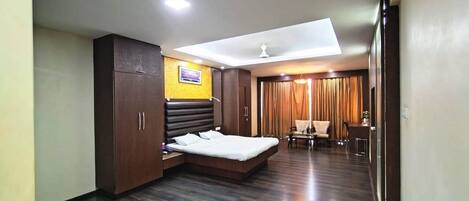 A modern hotel room with a large bed, a wardrobe, a desk, and a seating area with curtains.