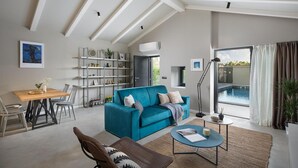 Una sala de estar moderna con un sofá azul aguamarina, un comedor con una mesa y sillas de madera, una estantería y vista a una piscina al aire libre.