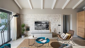 Una sala de estar moderna con una pared de piedra, un ventanal grande, una mesa redonda azul, una lámpara de pie y un sillón cómodo.