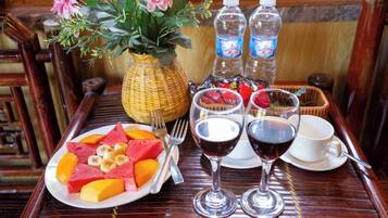 A wooden table with a plate of fruit, two wine glasses, a vase with flowers, and two water bottles.