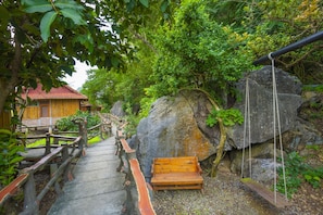 A wooden bench and swing set in a forested area with a stone pathway leading to a building with a red roof. - Lotus Field Homestay (Hoa Lu)