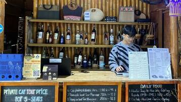 A wooden bar area with a bamboo ceiling, shelves of bottled beverages, and a menu board.