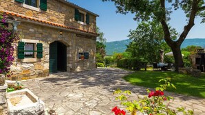 A stone building with a sign reading "ROMANA" and a stone pathway leading to a grassy area with outdoor seating.