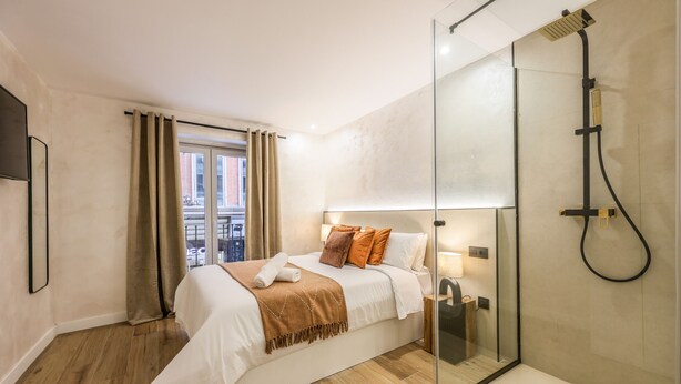 A modern hotel room with a large bed, a glass shower enclosure, and a view of the city through the window. - NEW loft one step away from SOL (P1B) (Madrid)
