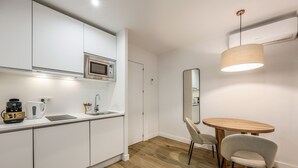 A modern kitchen with white cabinets, a microwave, and a coffee maker. There is a round wooden table with two chairs and a hanging light fixture.