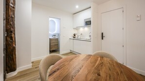 A modern kitchen with white cabinets, a microwave, and a sink. There is a wooden dining table with chairs.