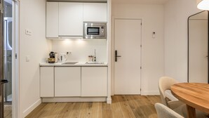 A compact kitchen with white cabinets, a microwave, a coffee maker, and a wooden dining table with chairs.