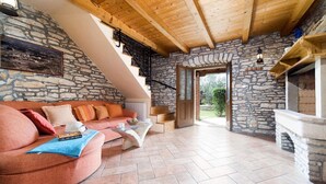 A cozy living room with a stone wall, a wooden ceiling, a pink sofa, a glass coffee table, and a fireplace. - Beautiful home in Marcana (Marcana)