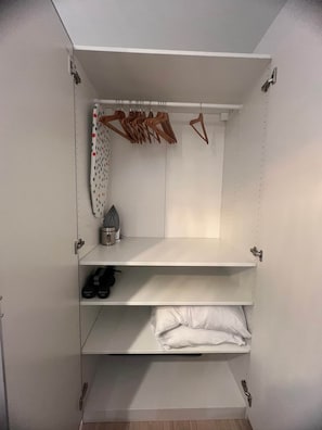 Une armoire blanche dotée de plusieurs étagères, d’une tringle pour suspendre les vêtements et d’un petit espace de rangement.