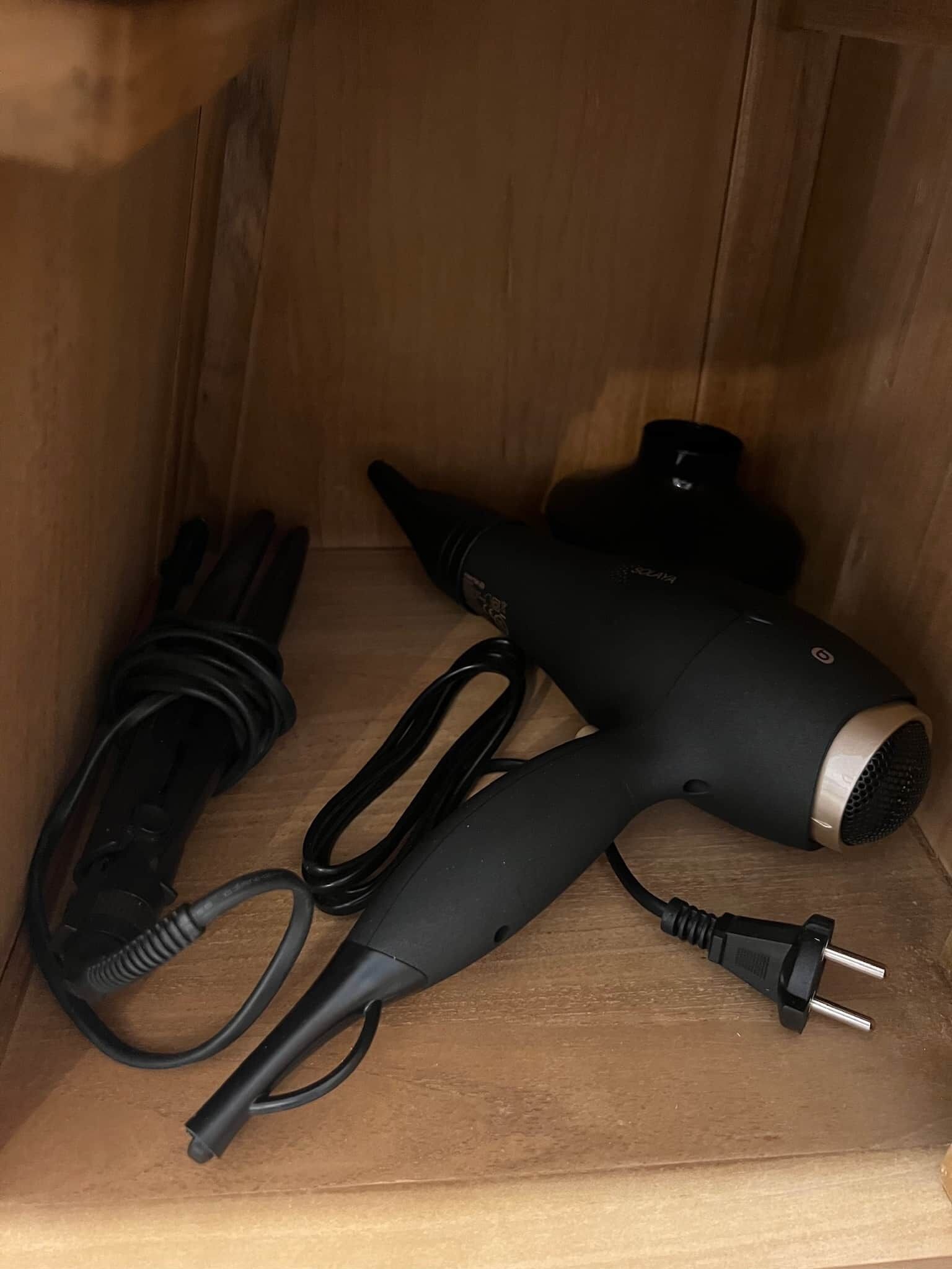 A wooden cabinet with a hair dryer and its power cord inside.