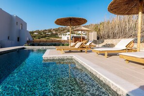 A pool with clear blue water, wooden lounge chairs, and thatched umbrellas.