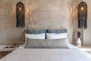 A bed with white and grey bedding, a magazine on the bedside table, and a vase with flowers on the nightstand.