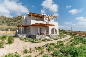 A two-story house with a stone foundation, wooden pergola, and a paved patio.