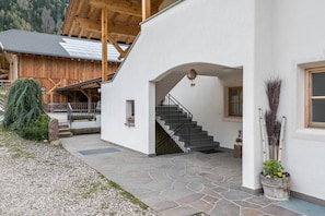 Un bâtiment dont l’entrée est pavée de pierres, avec un escalier et une structure en bois en arrière-plan.