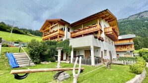 A two-story chalet with wooden balconies, a ski lift, and a mountain backdrop.