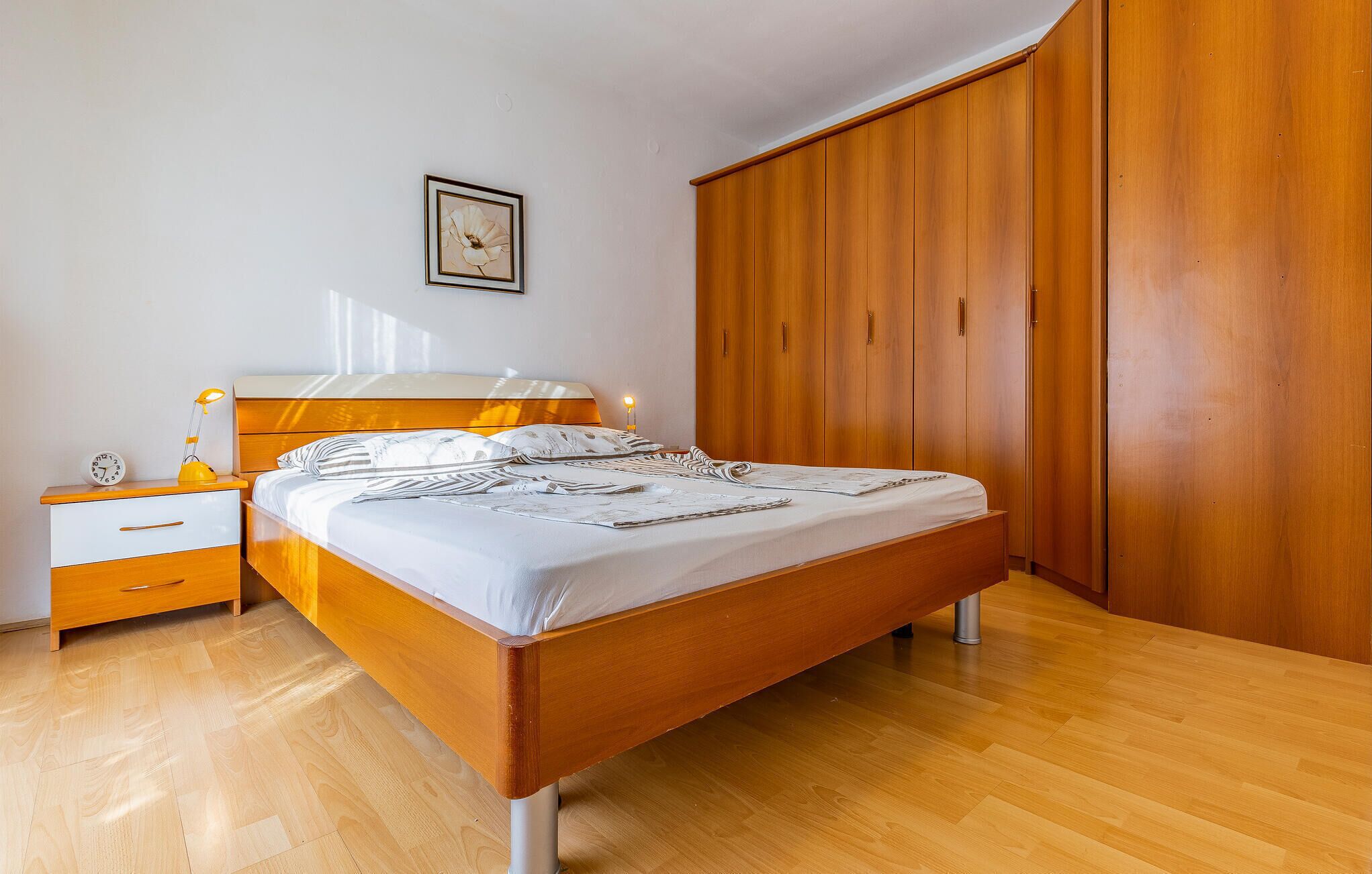 Et soveværelse med en træseng, et natbord med en lampe, et sengebord og en garderobe.