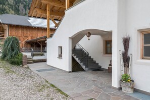 A modern building with a stone-paved entrance, a wooden staircase, and a view of a mountain.