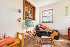 Una habitación con un caballete de madera, una mecedora, un sofá con cojines y una ventana decorada con motivos de corazón.