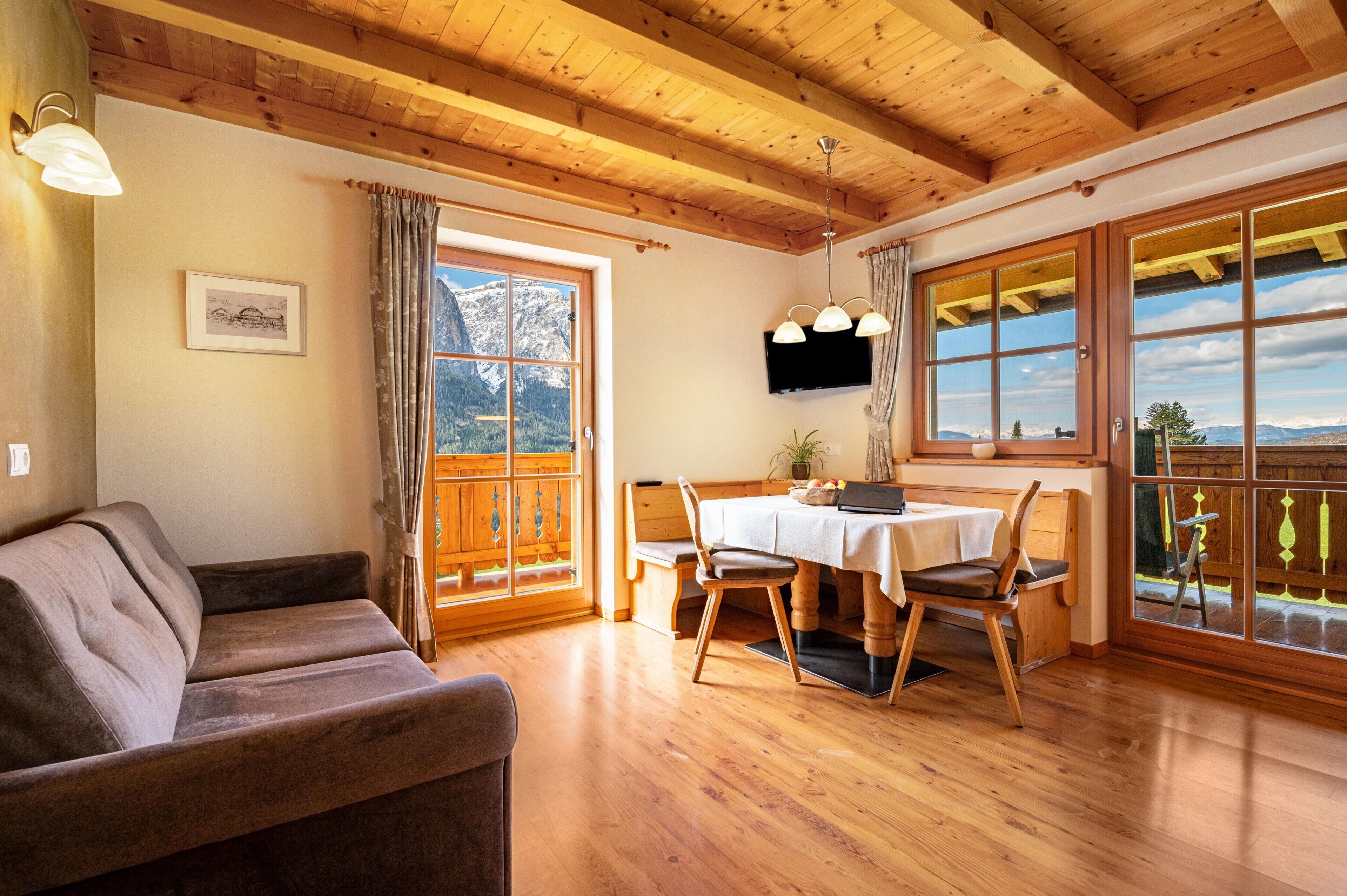 Un intérieur en bois comprenant un canapé, une table à manger, des chaises, un téléviseur et de grandes fenêtres offrant une vue sur la montagne.