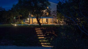 Una casa moderna con fachada de piedra, un gran árbol en el frente y un área exterior bien iluminada con piscina.