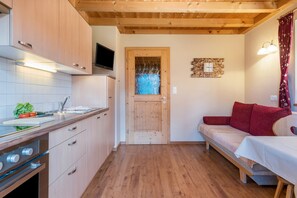 A compact kitchen with wooden cabinets, a built-in oven, and a small dining area with a table and red cushions.