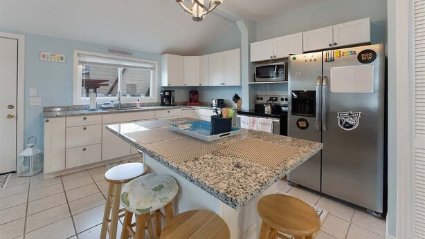 Una cocina con una isla central, armarios blancos, un refrigerador de acero inoxidable y una araña.