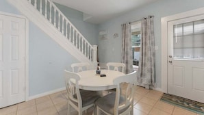 Un área de comedor con una mesa y sillas blancas, una escalera y una puerta con ventanal.